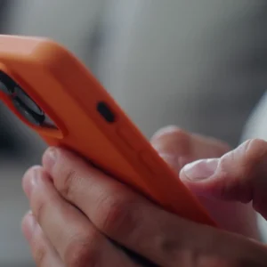 Person holding and using an orange smartphone.
