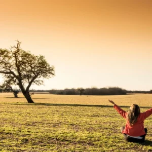 Person pointing toward the horizon in a vast field at sunset.